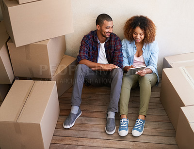 Buy stock photo Shot of a young couple using a tablet while sitting among boxes on moving day