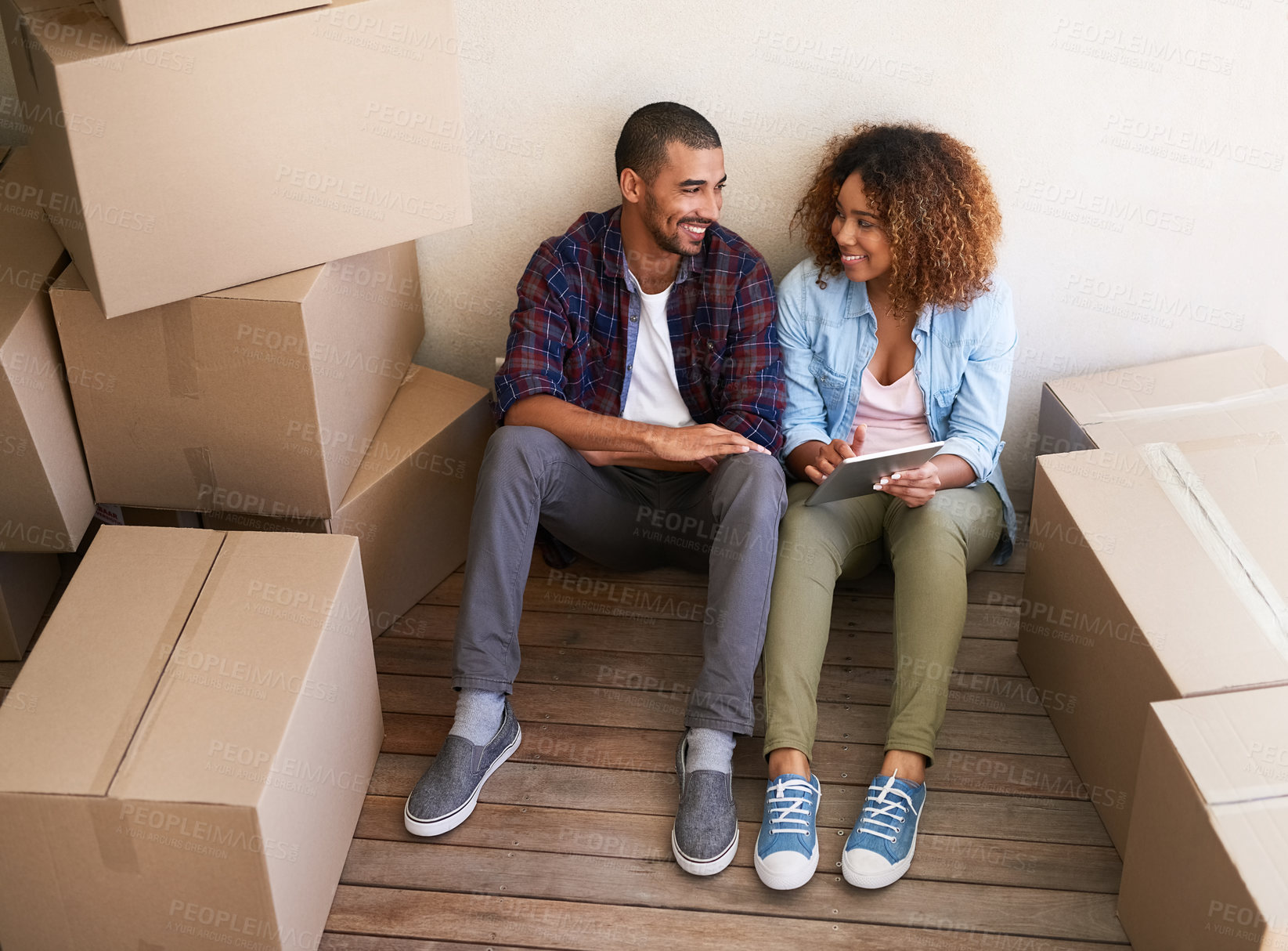 Buy stock photo Shot of a young couple using a tablet while sitting among boxes on moving day