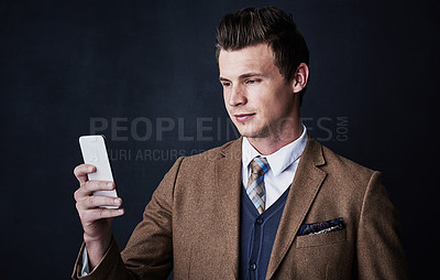 Buy stock photo Studio shot of a young businessman using his cellphone against a dark background