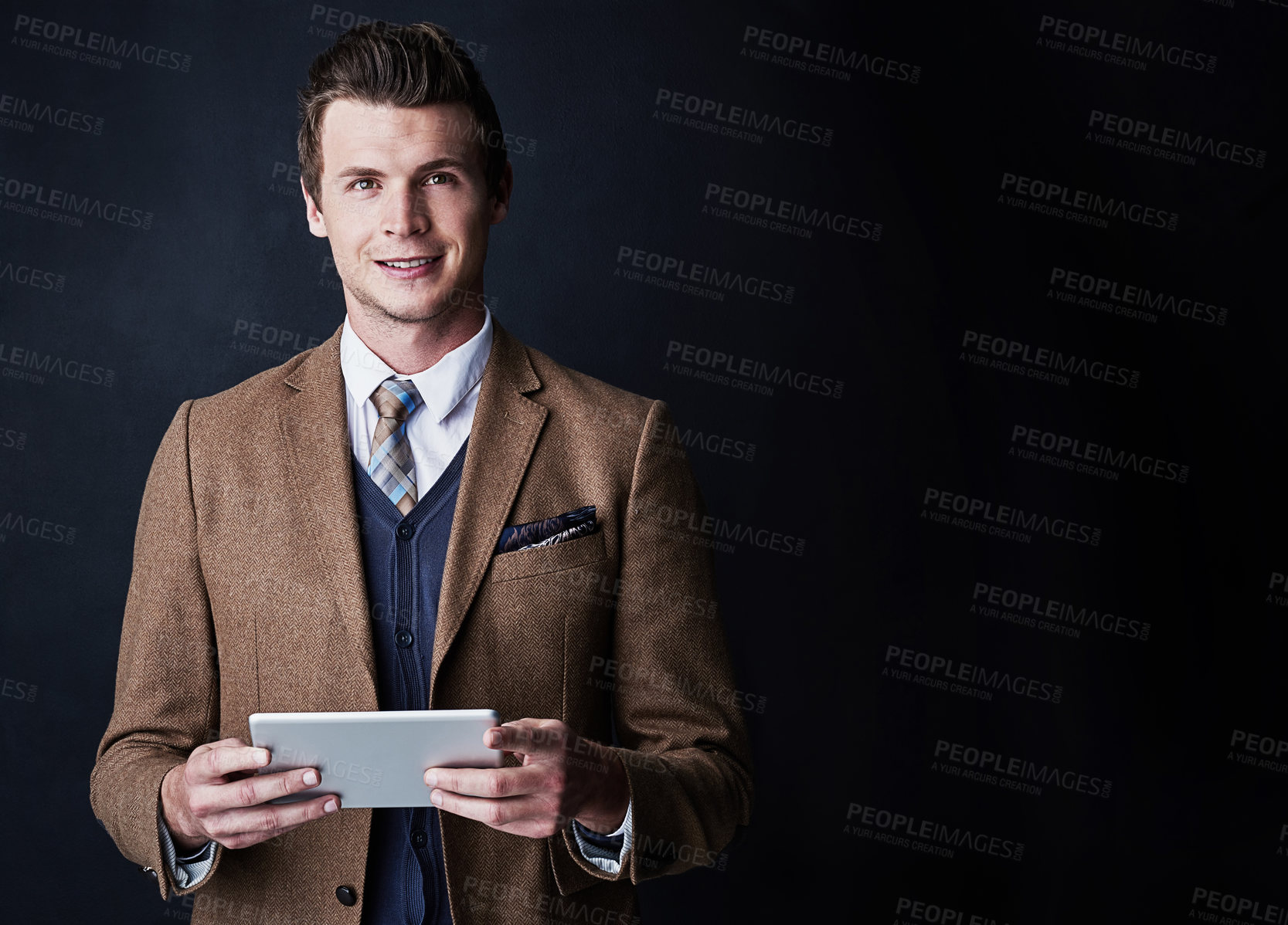 Buy stock photo Studio shot of a young businessman using his tablet against a dark background
