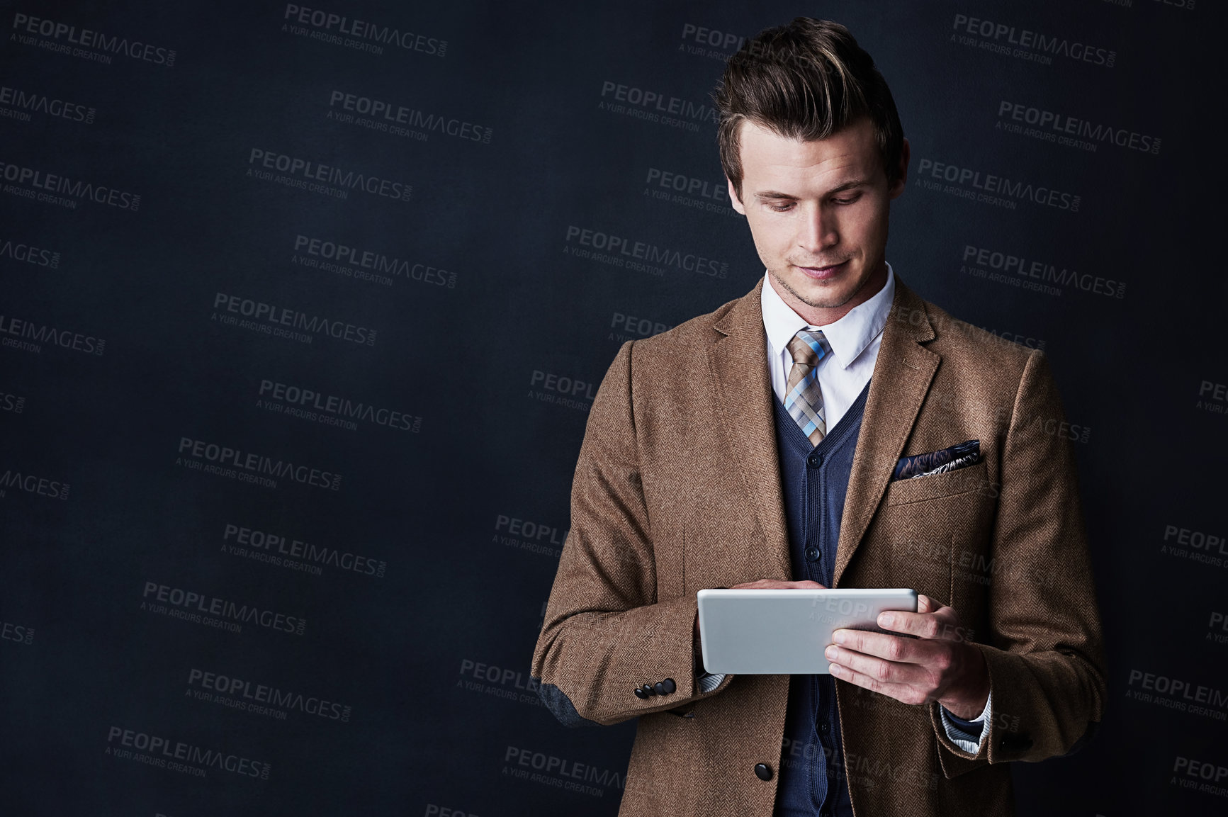 Buy stock photo Studio shot of a young businessman using his tablet against a dark background