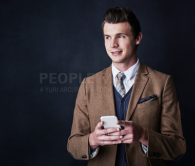 Buy stock photo Studio shot of a young businessman using his cellphone against a dark background
