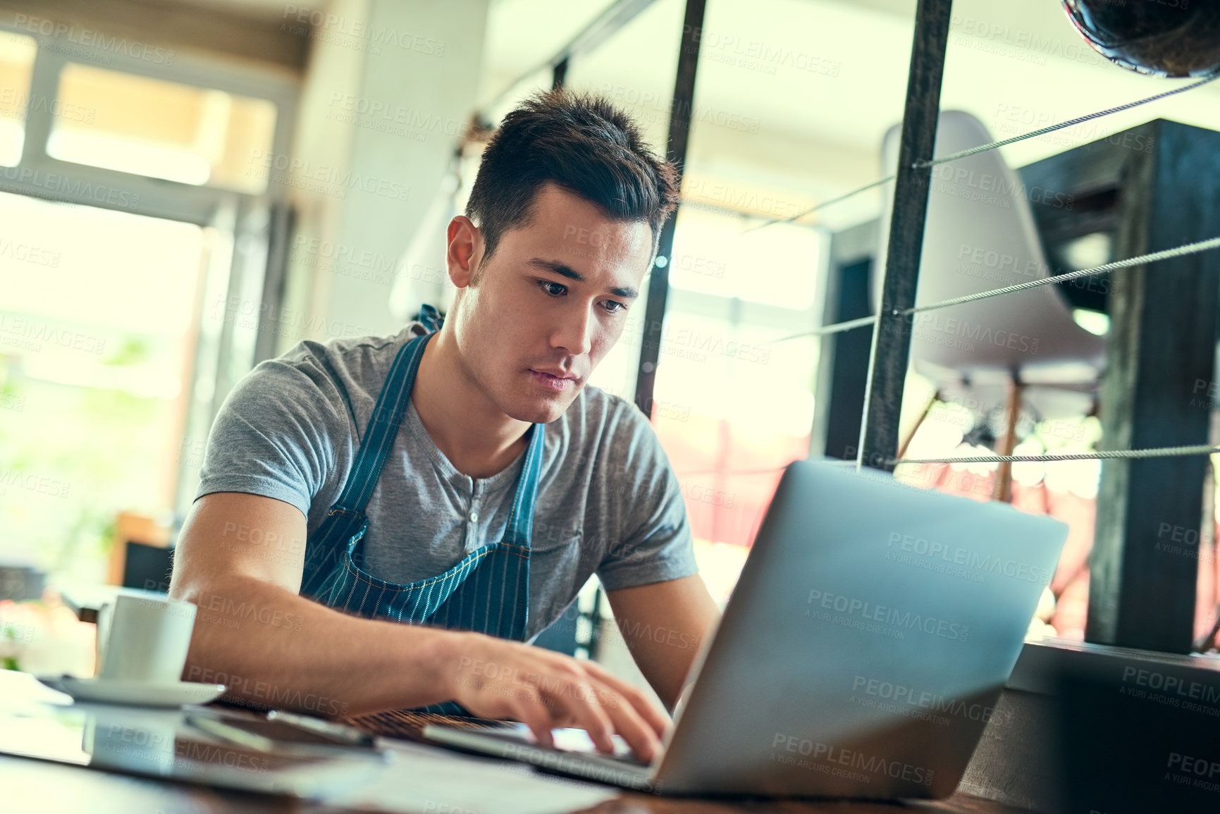 Buy stock photo Cropped shot of a young man working on a laptop in his coffee shop