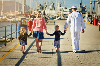 Buy stock photo Rearview shot of a family with young children walking along a harbor while holding hands