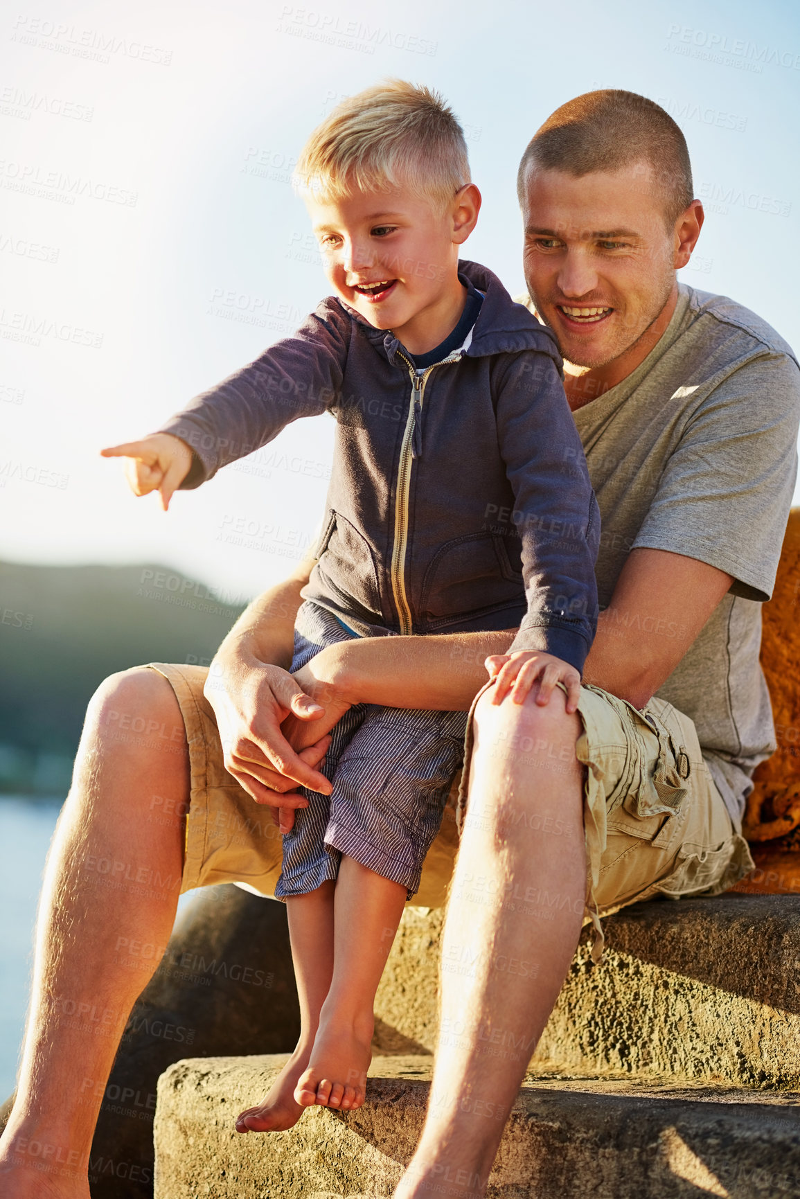 Buy stock photo Shot of a father bonding with his little boy while they sit by the harbor