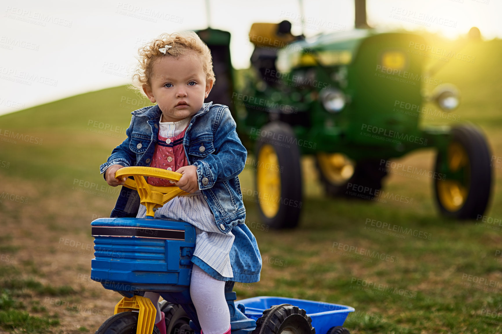 Buy stock photo Portrait, kid and driving toy tractor on farm in countryside for learning agriculture outdoor in nature. Girl, child and riding truck on grass for growth, development and farmer play on summer field