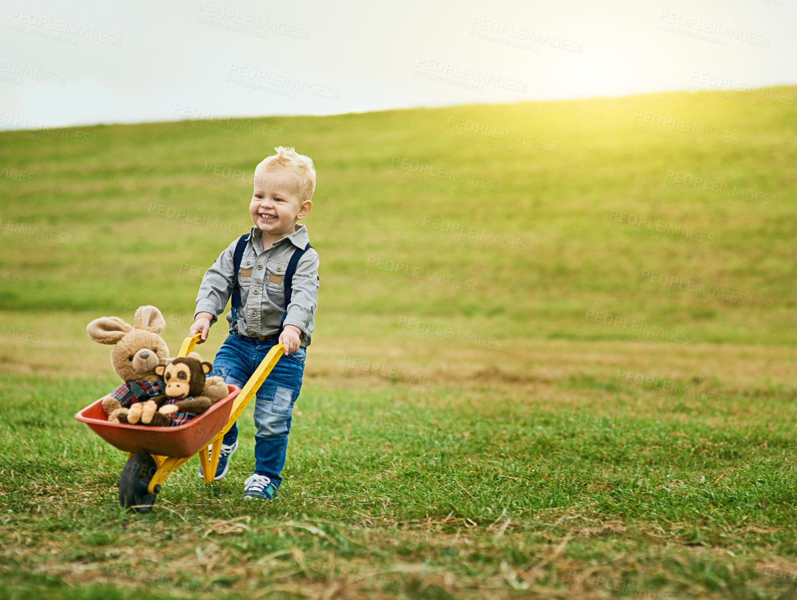 Buy stock photo Shot of an adorable little boy pushing a toy wheelbarrow filled with stuffed animals on a farm