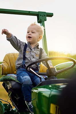 Buy stock photo Shot of an adorable little boy riding a tractor on a farm