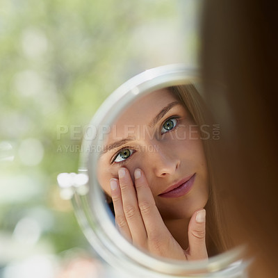 Buy stock photo Shot of an attractive young woman touching her skin in front of the mirror