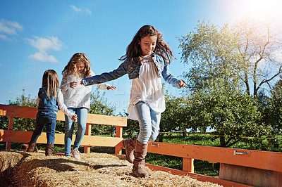 Buy stock photo Shot of three young sisters playing together on a bale of hay outdoors