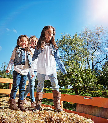 Buy stock photo Portrait of three young sisters playing together on a bale of hay outdoors