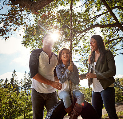 Buy stock photo Shot of a happy mother and  father pushing their daughter on a tyre swing