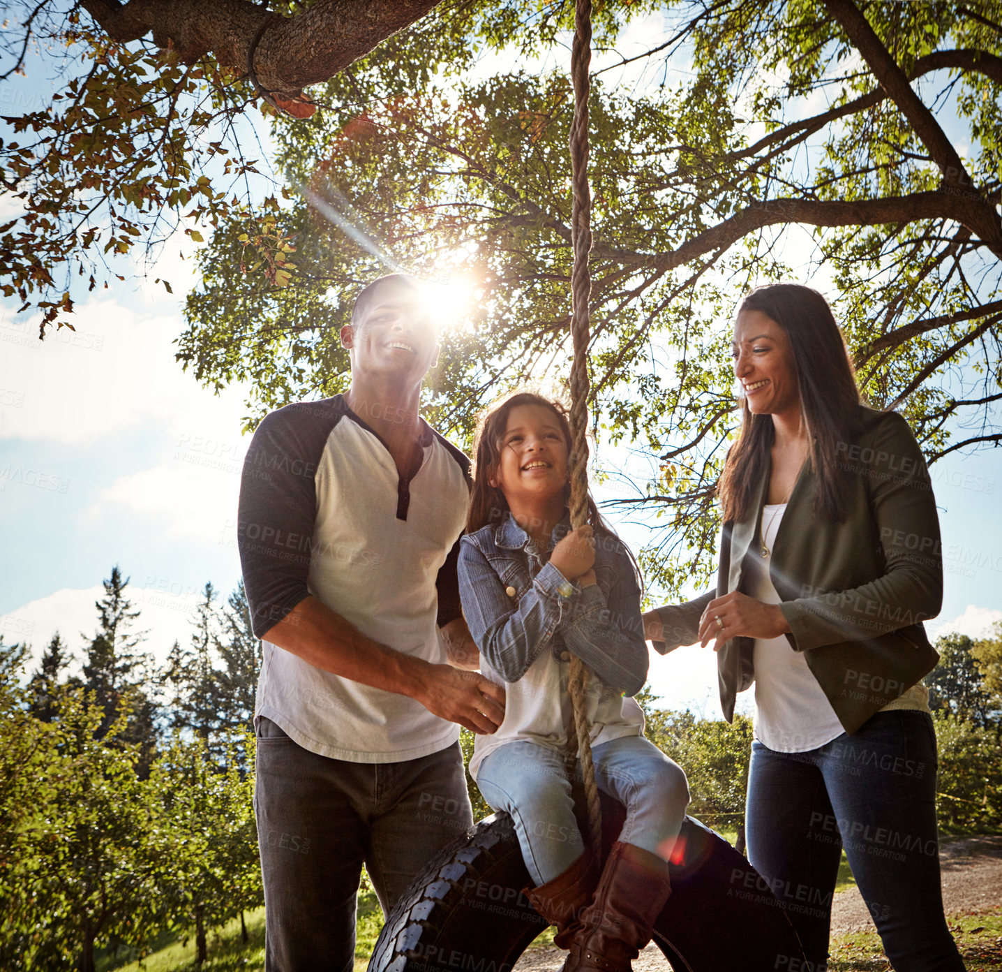 Buy stock photo Shot of a happy mother and  father pushing their daughter on a tyre swing