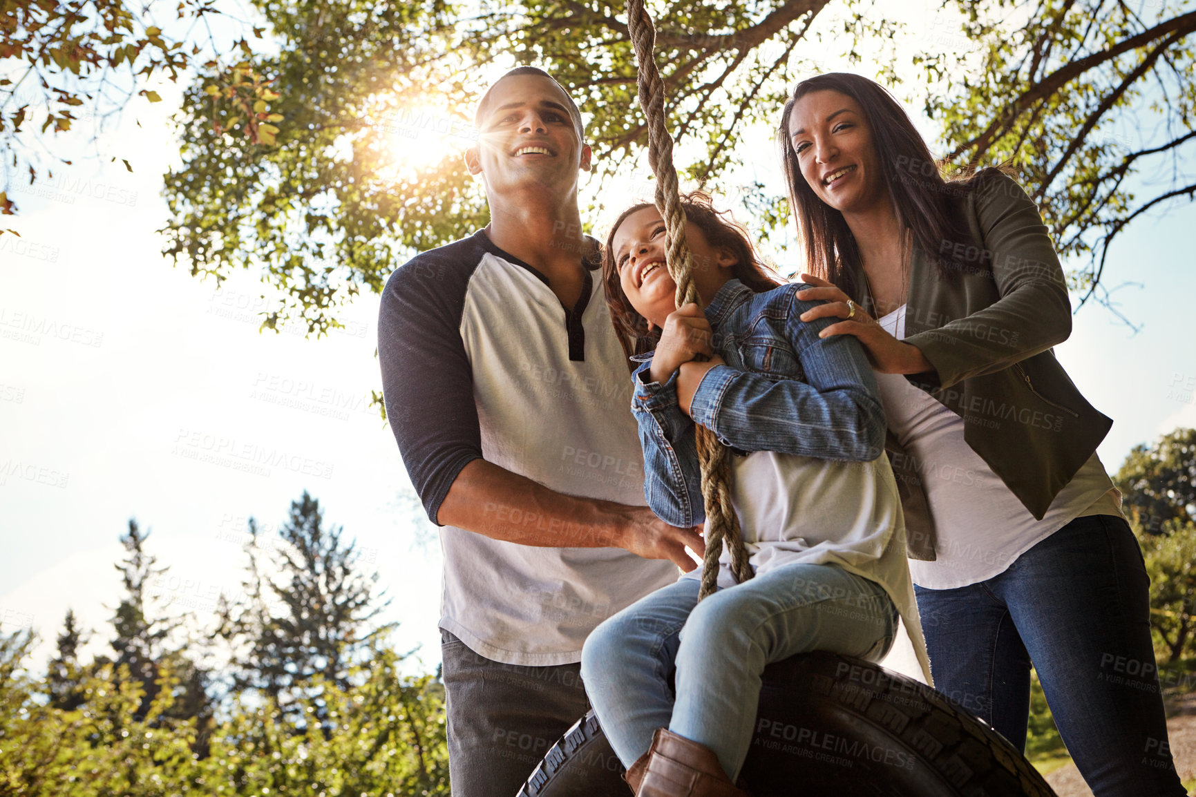 Buy stock photo Portrait of a happy mother and  father pushing their daughter on a tyre swing