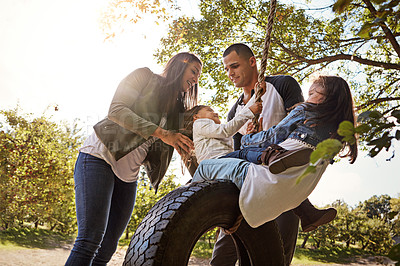 Buy stock photo Shot of a happy mother and  father pushing their daughters on a tyre swing