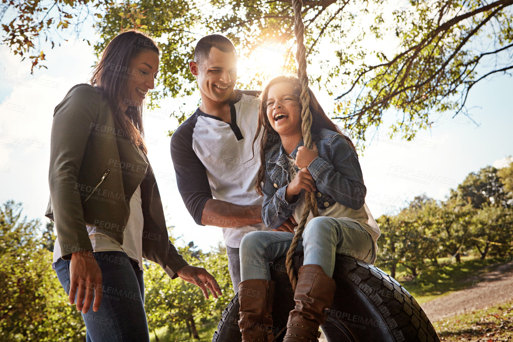 Buy stock photo Shot of a happy mother and  father pushing their daughter on a tyre swing