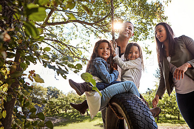 Buy stock photo Shot of a happy mother and  father pushing their daughters on a tyre swing