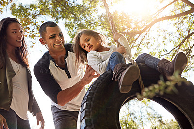 Buy stock photo Shot of a happy mother and  father pushing their daughter on a tyre swing