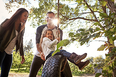 Buy stock photo Shot of a happy mother and  father pushing their daughter on a tyre swing