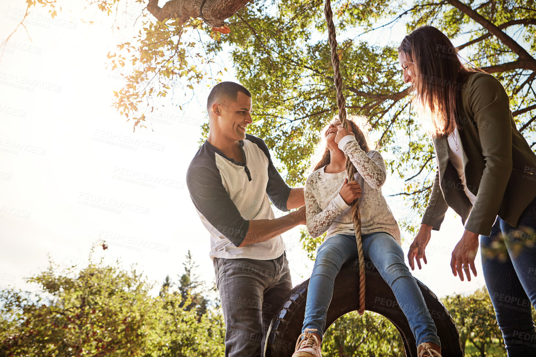 Buy stock photo Shot of a happy mother and  father pushing their daughter on a tyre swing