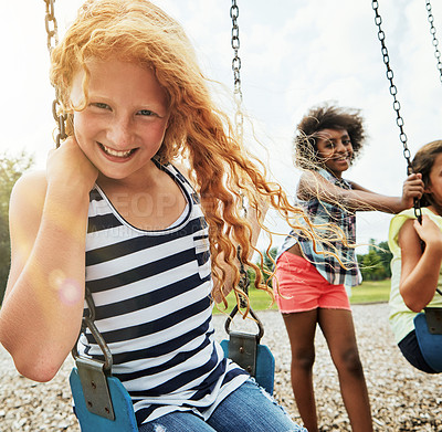 Buy stock photo Portrait of a young girl playing on a swing at the park with her friends