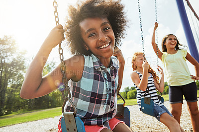 Buy stock photo Portrait of a young girl playing on a swing at the park with her friends