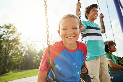 Buy stock photo Portrait of a young boy playing on a swing at the park with his friends