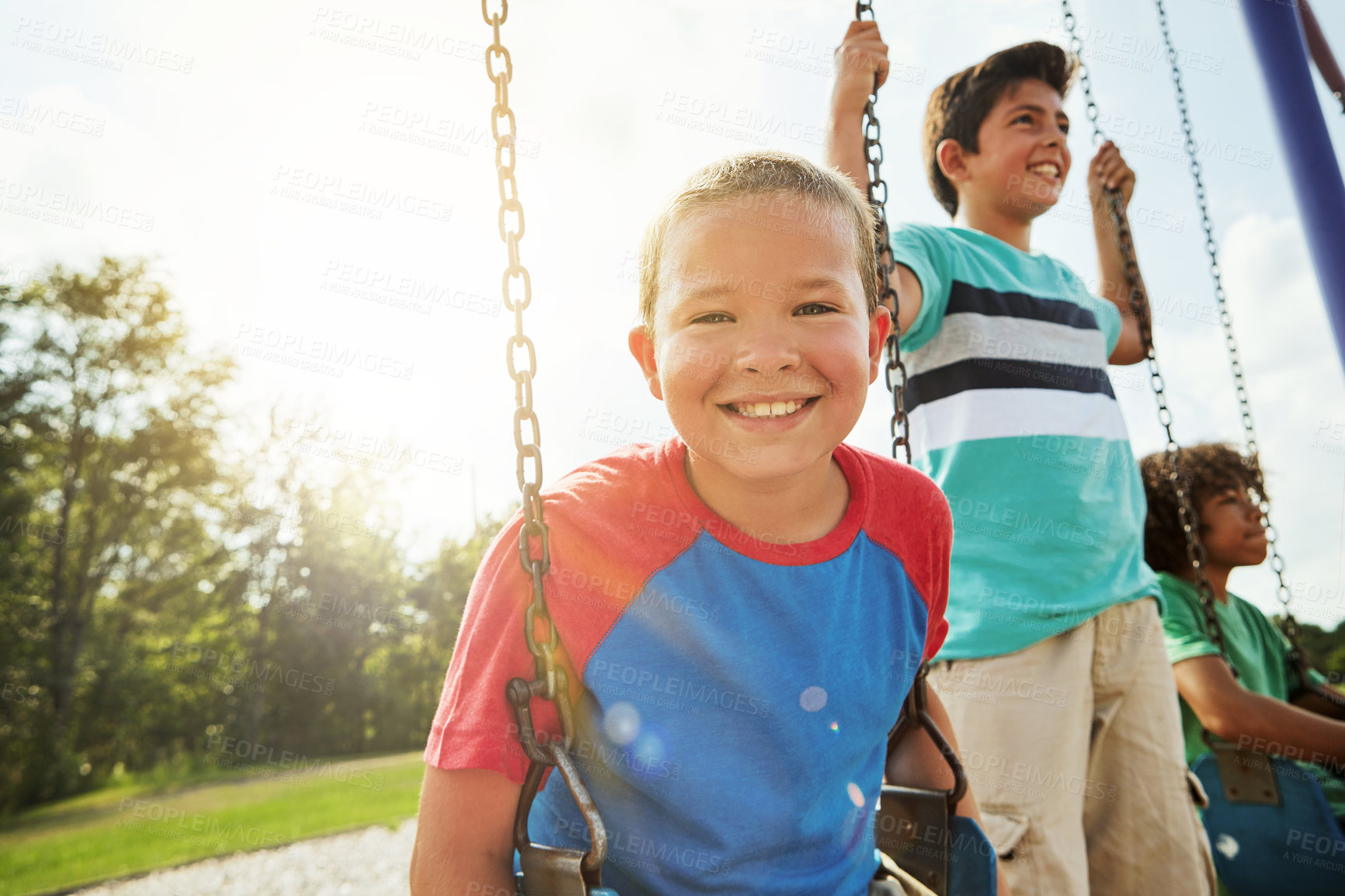 Buy stock photo Portrait of a young boy playing on a swing at the park with his friends