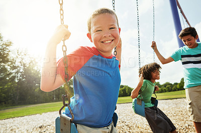 Buy stock photo Portrait of a young boy playing on a swing at the park with his friends