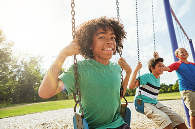 Buy stock photo Portrait of a young boy playing on a swing at the park with his friends