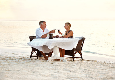 Buy stock photo Shot of a mature couple enjoying a romantic dinner on the beach