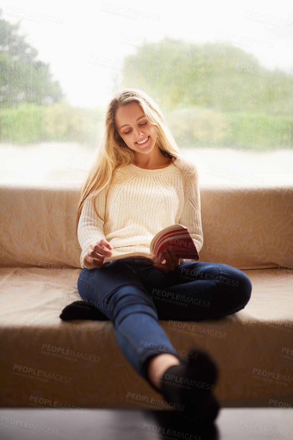 Buy stock photo Shot of an attractive young woman reading a book while sitting on the sofa at home
