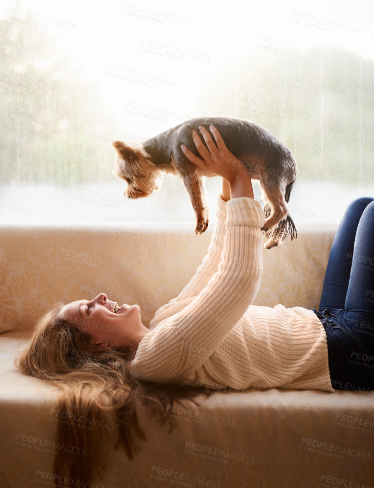 Buy stock photo Shot of an attractive young woman playing with her puppy while lying on the sofa at home