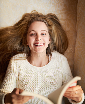 Buy stock photo Portrait of an attractive young woman reading a book while lying on the sofa at home