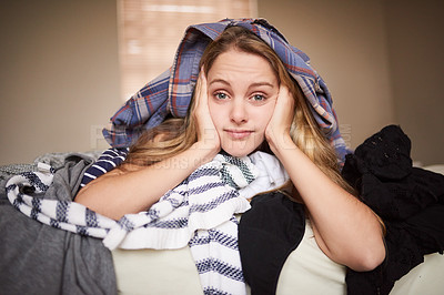 Buy stock photo Portrait of a bored-looking young woman lying underneath laundry on her bed