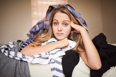Buy stock photo Portrait of a bored-looking young woman lying underneath laundry on her bed