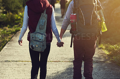 Buy stock photo Rearview shot of a young couple holding hands while walking along a hiking path