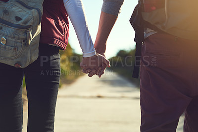 Buy stock photo Rearview shot of a young couple holding hands while walking along a hiking path