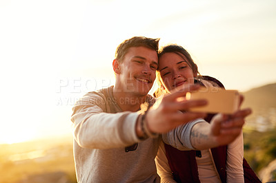 Buy stock photo Shot of a young couple taking a selfie while admiring the view from the top of a mountain