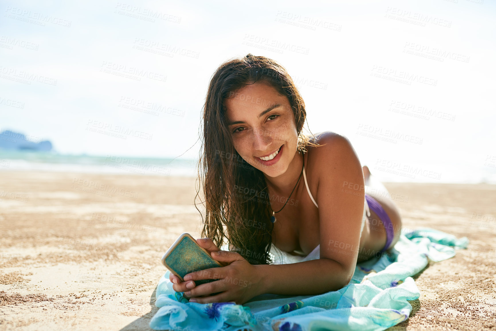Buy stock photo Shot of a beautiful young woman relaxing on the beach while using her phone