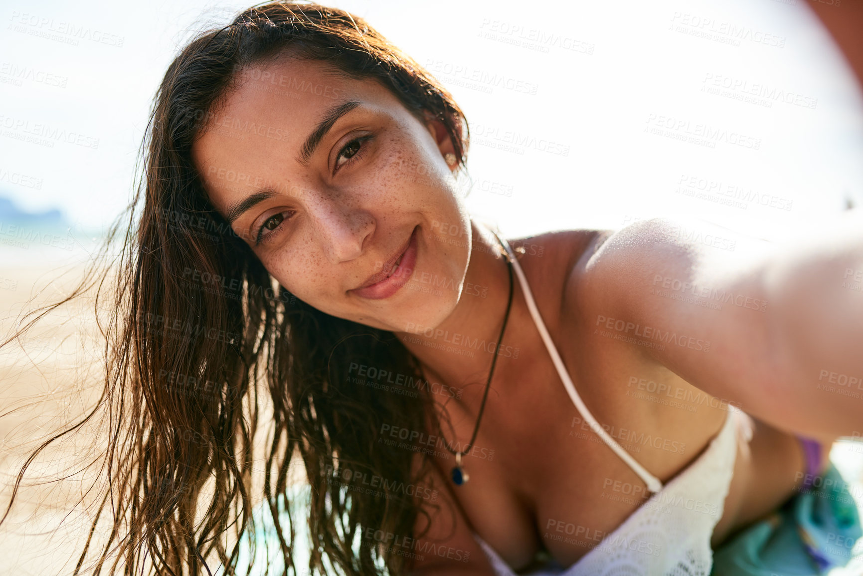 Buy stock photo Shot of a young woman taking a selfie while lying on the beach