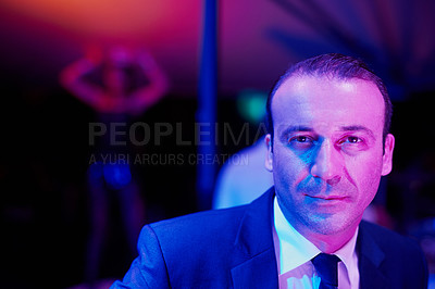 Buy stock photo Portrait of a seedy businessman in a go go bar with a woman dancing on a pole behind him