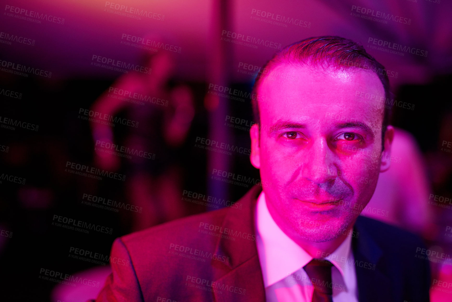 Buy stock photo Shot of a seedy businessman in a neon lit go go bar with a woman dancing on a pole behind him