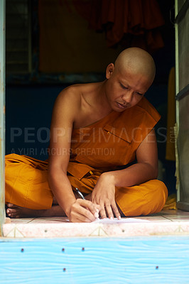 Buy stock photo Shot of a buddhist monk filling in a form while sitting in the doorway of his home