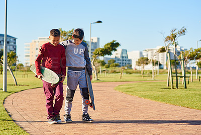 Buy stock photo Shot of two young brothers walking together with their skateboards at the park
