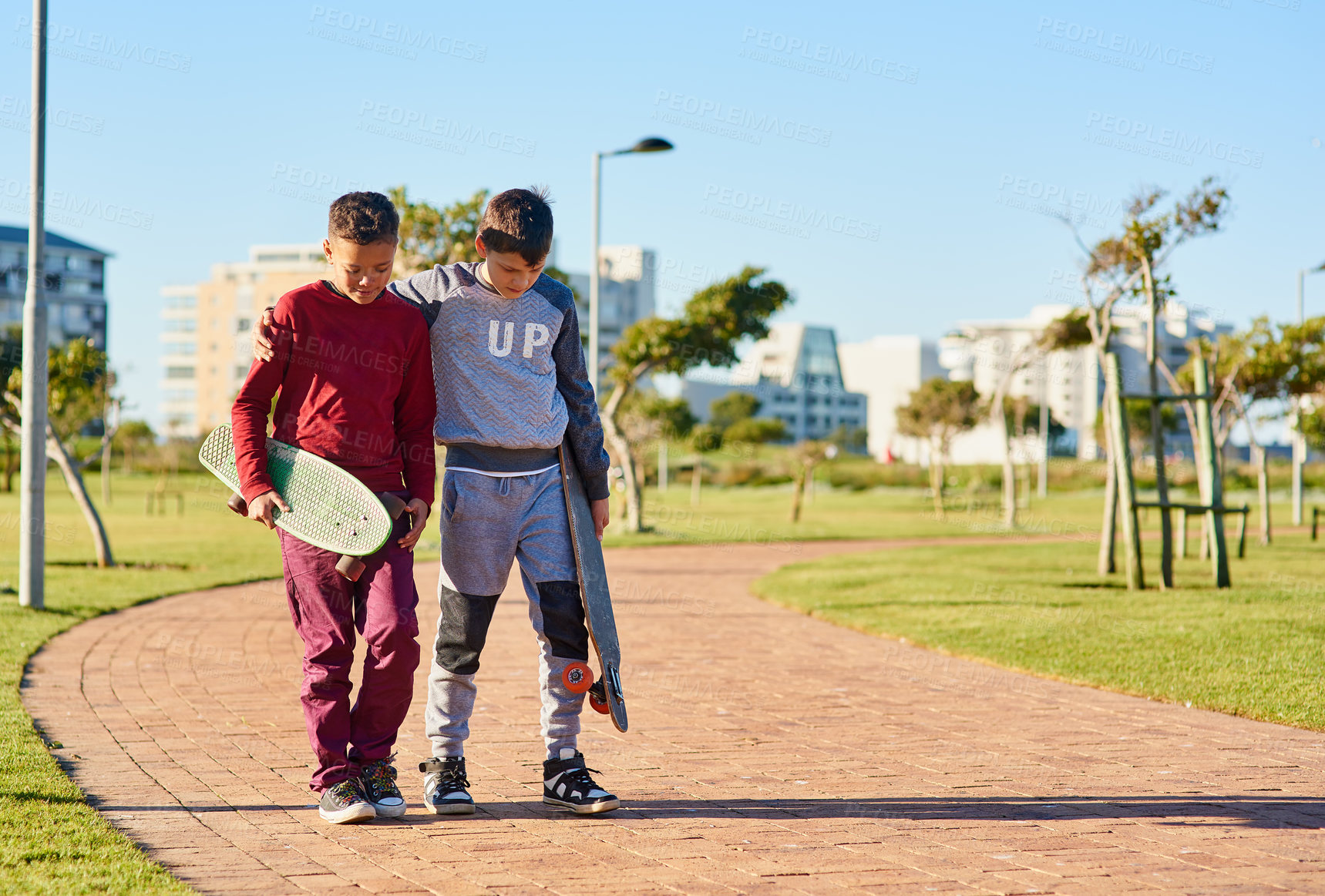 Buy stock photo Shot of two young brothers walking together with their skateboards at the park
