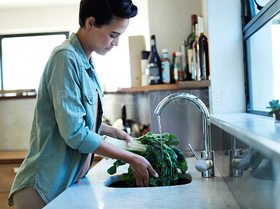 Buy stock photo Shot of a young woman washing vegetables in her kitchen sink