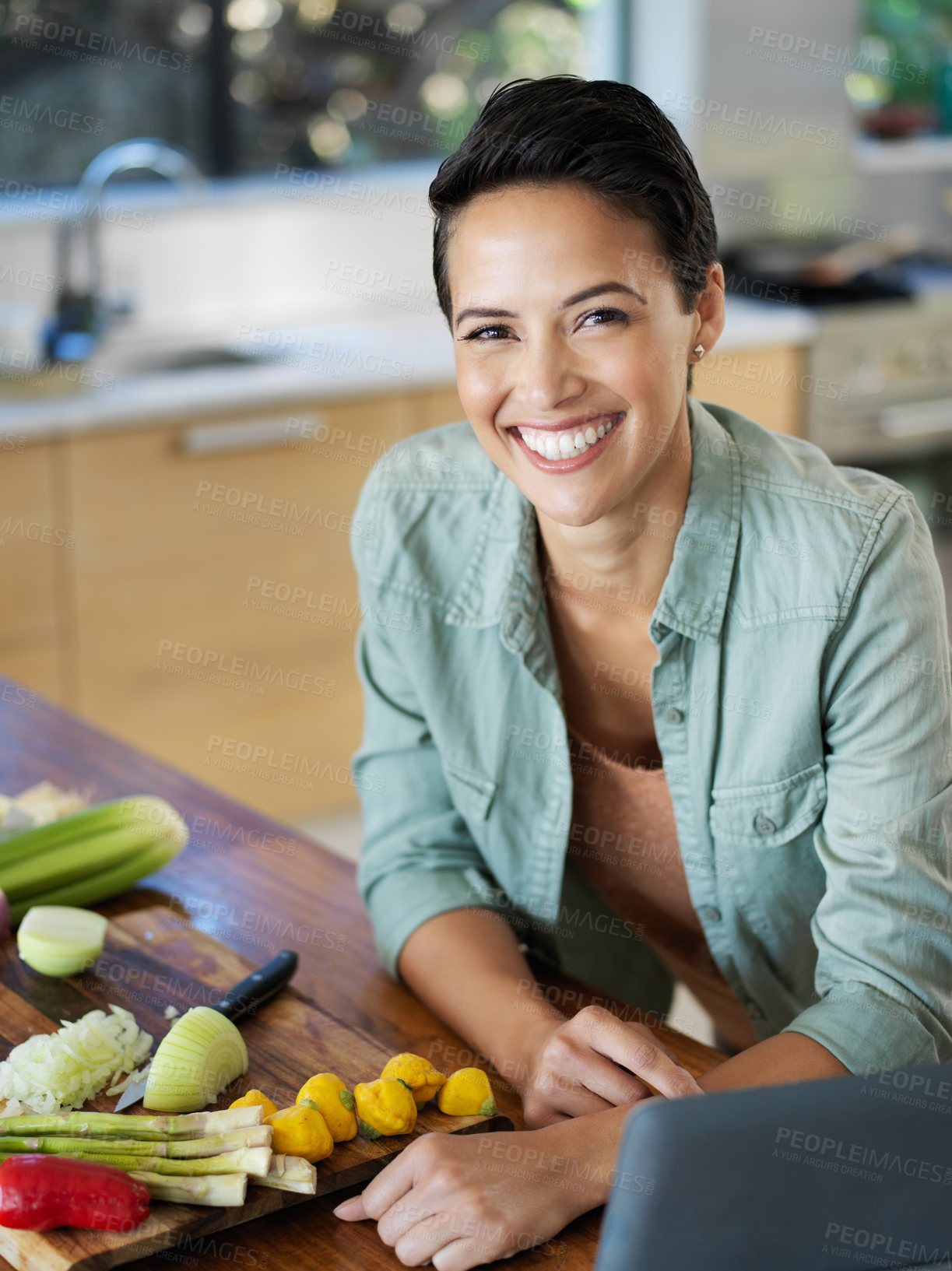 Buy stock photo Portrait of a smiling young woman using a digital tablet while preparing a meal in her kitchen