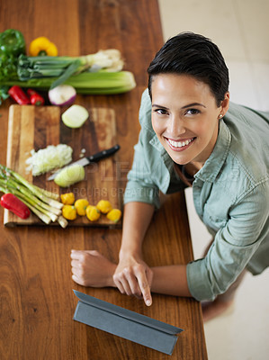Buy stock photo Portrait of a smiling young woman using a digital tablet while preparing a meal in her kitchen