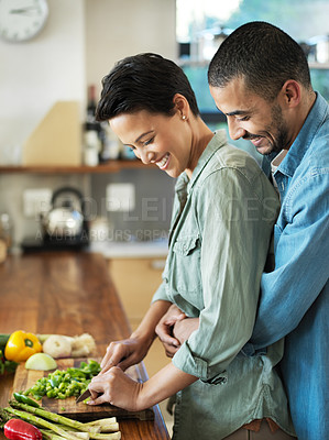 Buy stock photo Shot of an affectionate young couple preparing a meal together in their kitchen